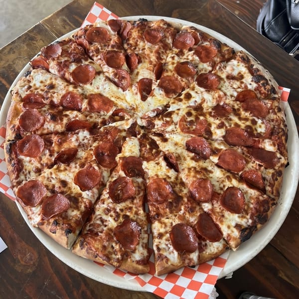 A large, sliced pepperoni pizza with melted cheese on a white plate with red and white checkered paper.
