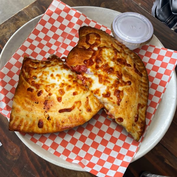 Two golden-brown calzones with melted cheese and red sauce on a red and white checkered paper.