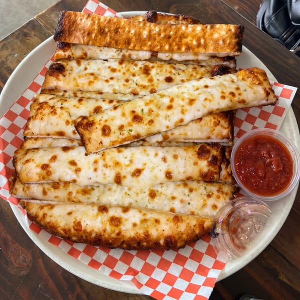 Cheesy garlic breadsticks with marinara sauce on a white plate with red and white checkered paper.