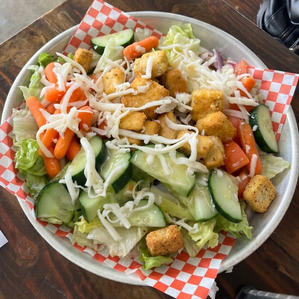 A salad with lettuce, carrots, cucumbers, tomatoes, cheese, and chicken nuggets in a metal bowl.