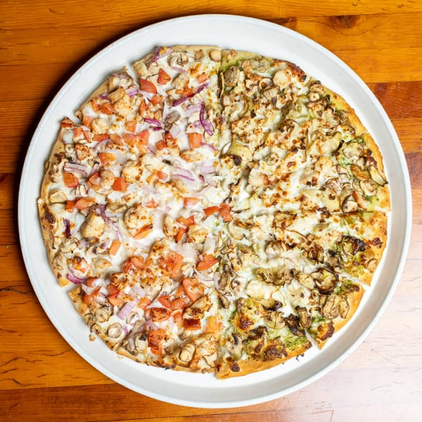 A large, round pizza with two distinct halves: one with tomatoes and red onions, the other with pesto and mushrooms.