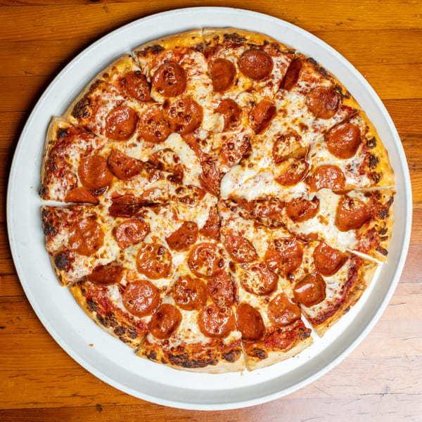 A whole pepperoni pizza, cut into slices, on a white tray atop a wooden table.