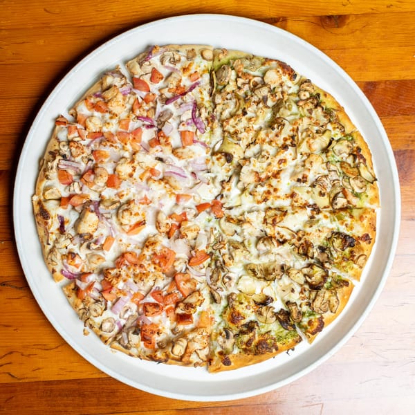 A large pizza with two distinct halves: one with chicken, tomatoes, and red onions, the other with mushrooms and pesto.
